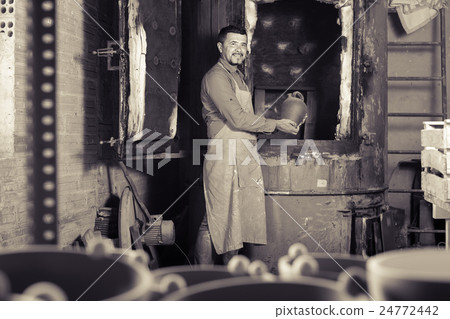 positive male with black-glazed ceramic vase standing close to kiln 24772442