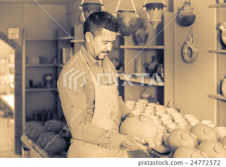 man potter holding ceramic vessels in atelier 24772572