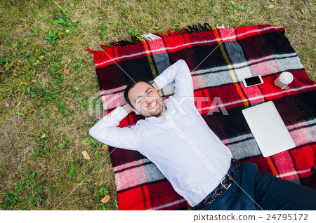 Happy young man with laptop relaxing on the grass Happy young man with laptop relaxing on the grass 24795172