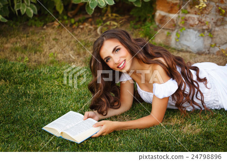 Girl reads book while lying on lawn. 24798896