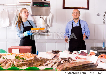 Young assistant offering fresh fish in shop 24826628