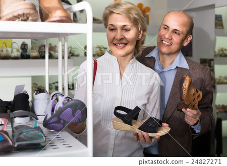 Two retirees together choosing pair of shoes in fashion store 24827271
