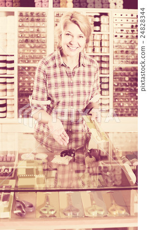 woman seller standing at counter with various scissors in sewing store 24828344