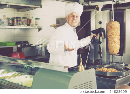 man chef wearing uniform cutting meat for kebab on kitchen in fa man chef wearing uniform cutting meat for kebab on kitchen in fa 24828609
