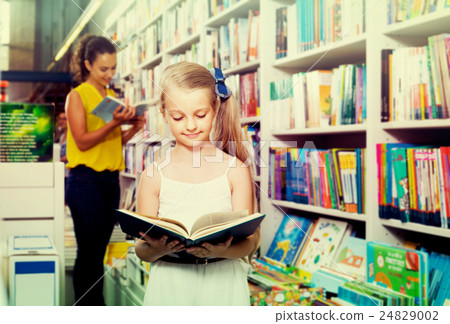 Glad girl in school age looking in open chosen book 24829002