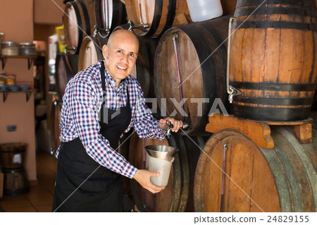 Cheerful man wine maker taking wine from wood Cheerful man wine maker taking wine from wood 24829155