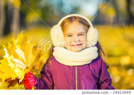 Happy little girl in earflaps with autumn leaves 24911649