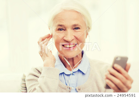 senior woman with smartphone and earphones at home senior woman with smartphone and earphones at home 24954591