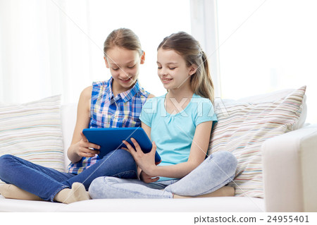 happy girls with tablet pc sitting on sofa at home happy girls with tablet pc sitting on sofa at home 24955401