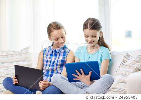 happy girls with tablet pc sitting on sofa at home happy girls with tablet pc sitting on sofa at home 24955405