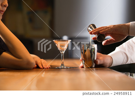 A cocktail-making bartender and a female customer A cocktail-making bartender and a female customer 24958911