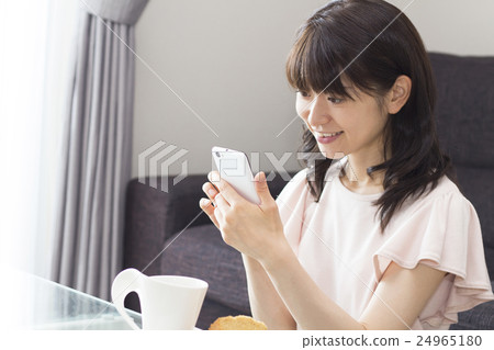 A woman who operates a smartphone while drinking tea in the living room A woman who operates a smartphone while drinking tea in the living room 24965180