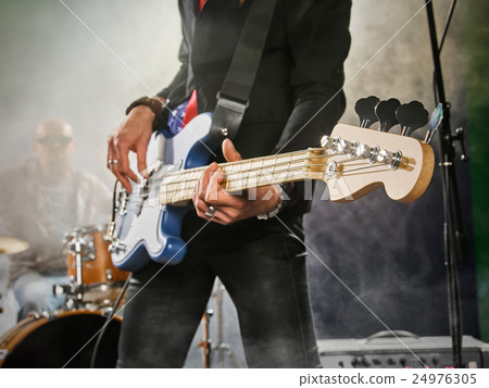 Rock band performs on stage. Bassist in the foreground. 24976305