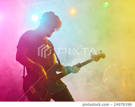 Rock band performs on stage. Bassist in the foreground. 24976396