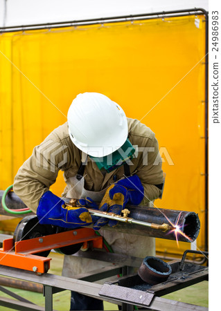 Welder cutting a pipe wearing protective clothes 24986983