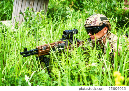 Military man sniper with automatic rifle with a telescopic sight lies in grass in forest 25004013