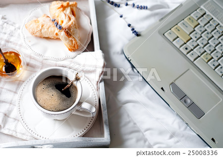 A cup of coffee with the laptop on the bed 25008336