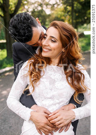 Groom kisses shining bride's face hugging Groom kisses shining bride's face hugging 25091375