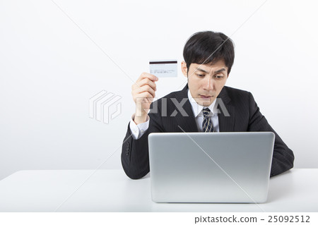 A businessman with a card in front of a personal computer A businessman with a card in front of a personal computer 25092512
