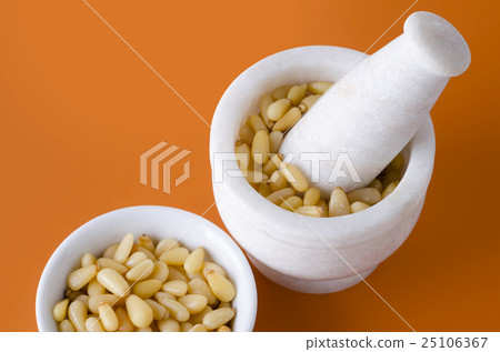 Shelled pine nuts in bowl and mortar over orange 25106367