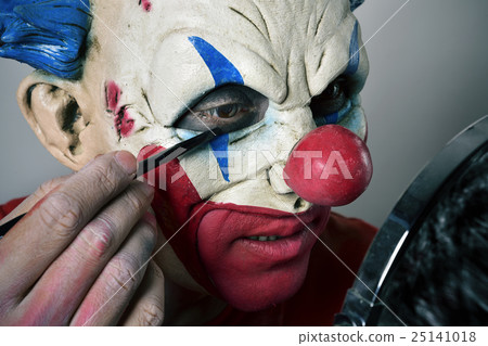 young man making up himself as an evil clown 25141018