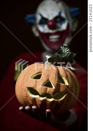 evil clown with a carved pumpkin 25141023