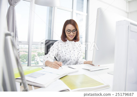 Smiling asian businesswoman at office desk writing Smiling asian businesswoman at office desk writing 25179687