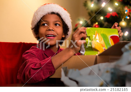 Smiling darkskinned boy unpacks present. Smiling darkskinned boy unpacks present. 25182185