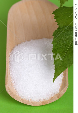 Xylitol birch sugar on wooden scoop over green 25239783
