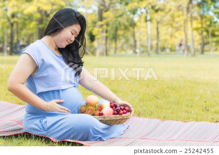 Pregnant woman holding belly and fruit in garden. Pregnant woman holding belly and fruit in garden. 25242455