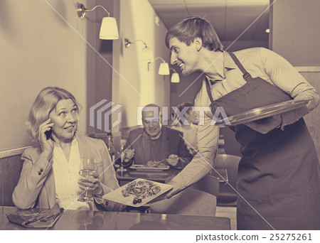 Positive waiter bringing order to happy charming mature female Positive waiter bringing order to happy charming mature female 25275261