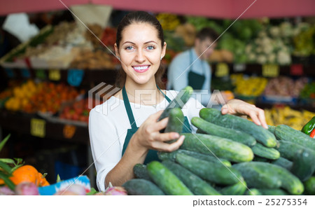 Stuff in apron selling green cucumber at marketplace 25275354