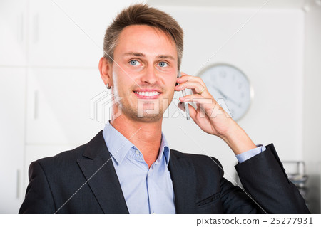 Happy man talking on mobile phone at office Happy man talking on mobile phone at office 25277931