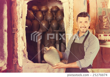 Cheerful craftsman carrying fresh baked black glazed vessel 25278874