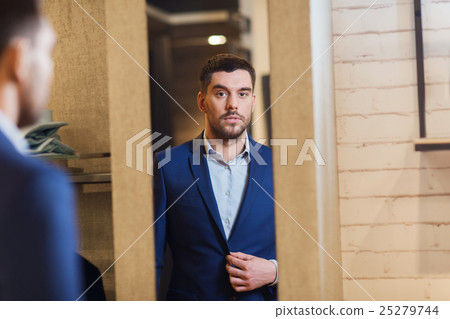 man trying jacket on at mirror in clothing store 25279744