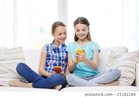 happy girls with smartphones sitting on sofa happy girls with smartphones sitting on sofa 25282260