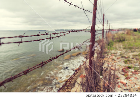 barb wire fence over gray sky and sea barb wire fence over gray sky and sea 25284814