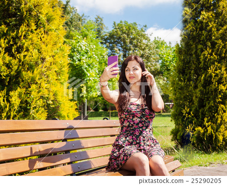 young girl making selfie sitting on a park bench 25290205