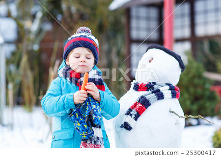Funny kid boy making a snowman in winter outdoors Funny kid boy making a snowman in winter outdoors 25300417