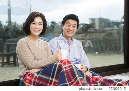 Middleaged Asian Couple Smiling and Sitting with Coffee Mugs on Rug In Livingroom Middleaged Asian Couple Smiling and Sitting with Coffee Mugs on Rug In Livingroom 25306945