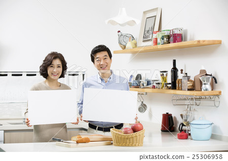 Middleaged Asian Couple Holding a Blank Board at Kitchen Counter 25306958