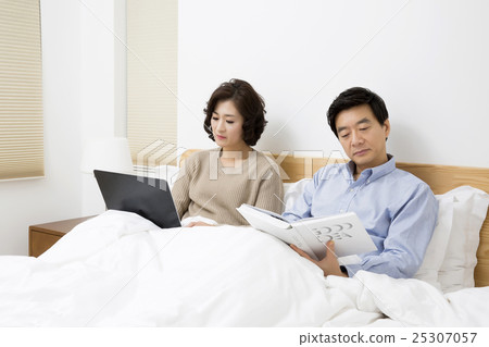 Middleaged Asain Couple in Bed, Wife Looking at a Laptop and Husband Reading Newspaper Middleaged Asain Couple in Bed, Wife Looking at a Laptop and Husband Reading Newspaper 25307057