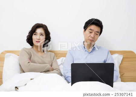 Middleaged Asian Couple Looking stressed in Bedroom with Laptop Middleaged Asian Couple Looking stressed in Bedroom with Laptop 25307141