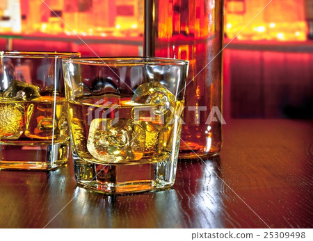 glasses of whiskey with ice on bar table near whiskey bottle on warm atmosphere 25309498