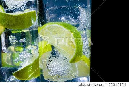 close-up of two glasses with cocktail and ice with lime slice on black background with space for text 25310154