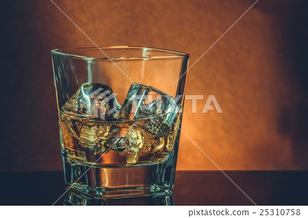 glass of whiskey on black table with reflection, warm atmosphere 25310758