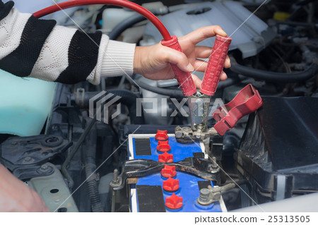 woman hand hold jumper cables to car battery woman hand hold jumper cables to car battery 25313505