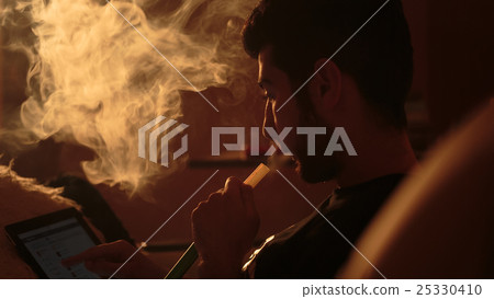 man smokes a hookah and uses tablet 25330410