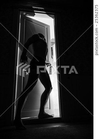 Young man stands near door in black room 25362375