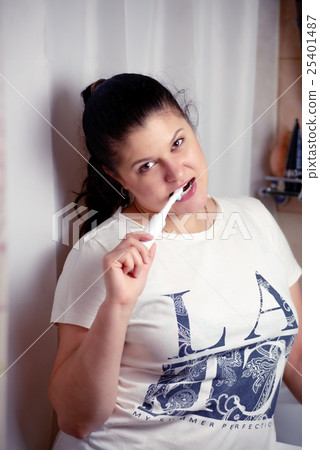 Young woman brushes teeth in bathroom an electric brush 25401487